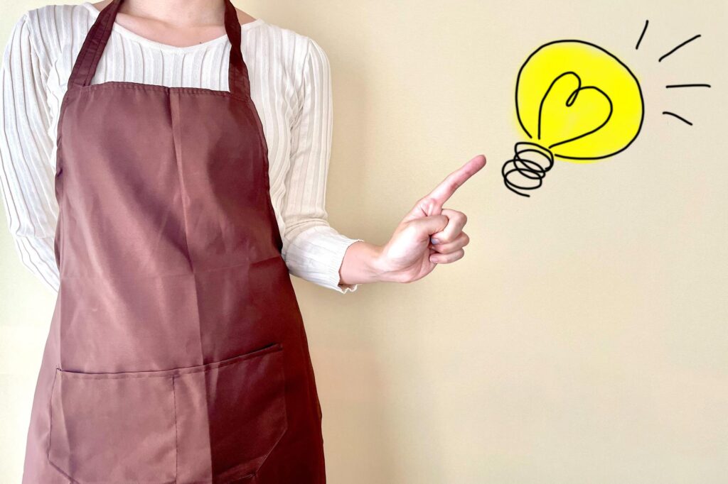 豆電球マークを指さすエプロンを付けた人
