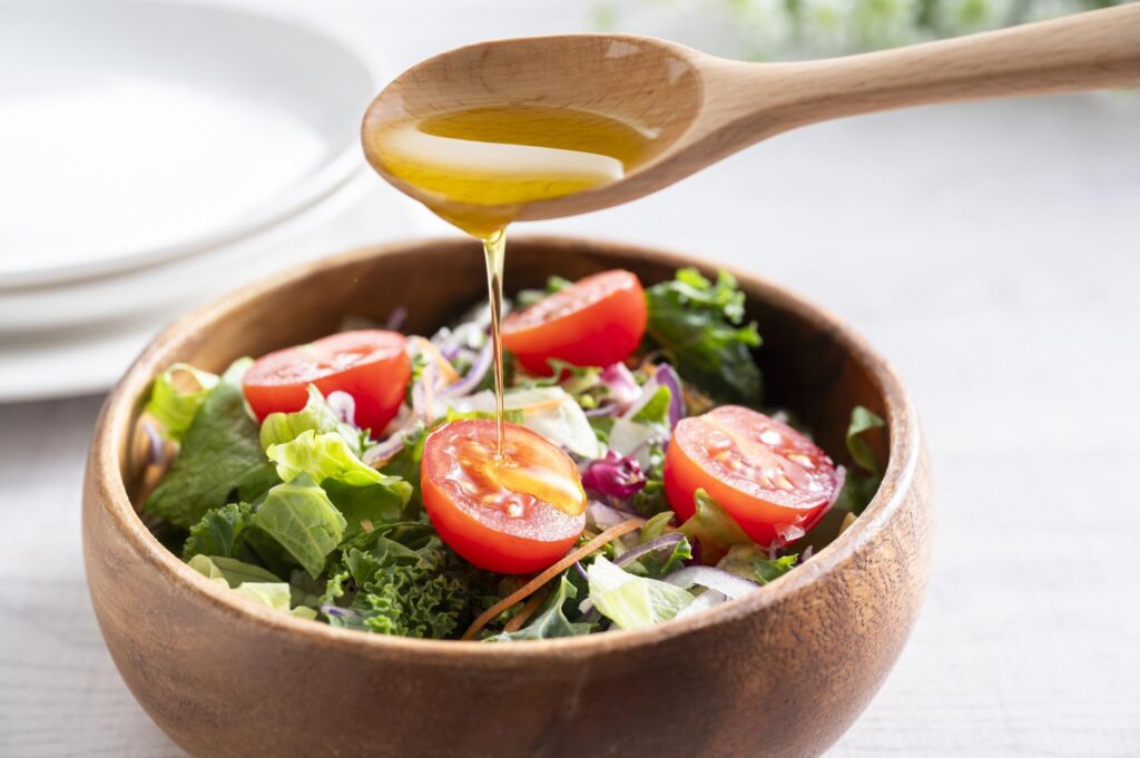スプーンを使ってサラダにオリーブオイルをかける様子